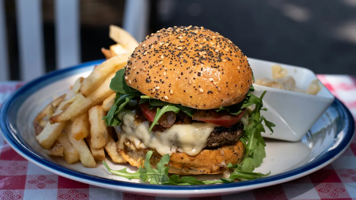 Juicy cheeseburger with sesame seed bun, lettuce, tomato, and fries on a white plate with blue rim.