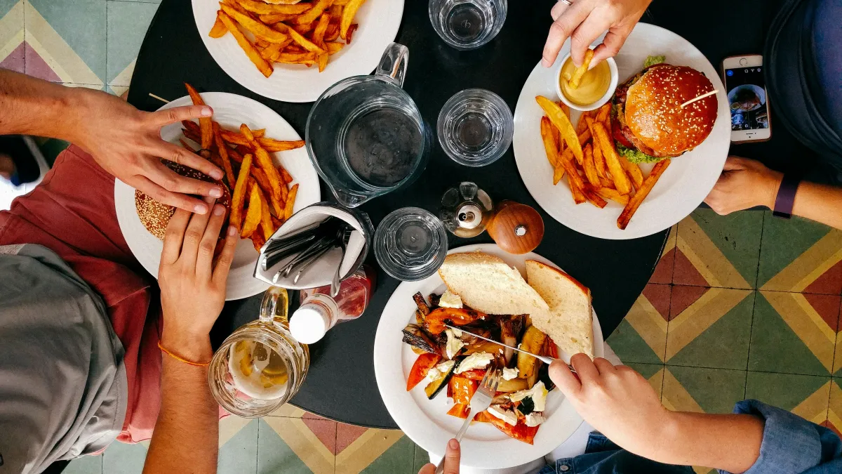 Top-down view of a table with burgers, fries, drinks, and people sharing a meal together.