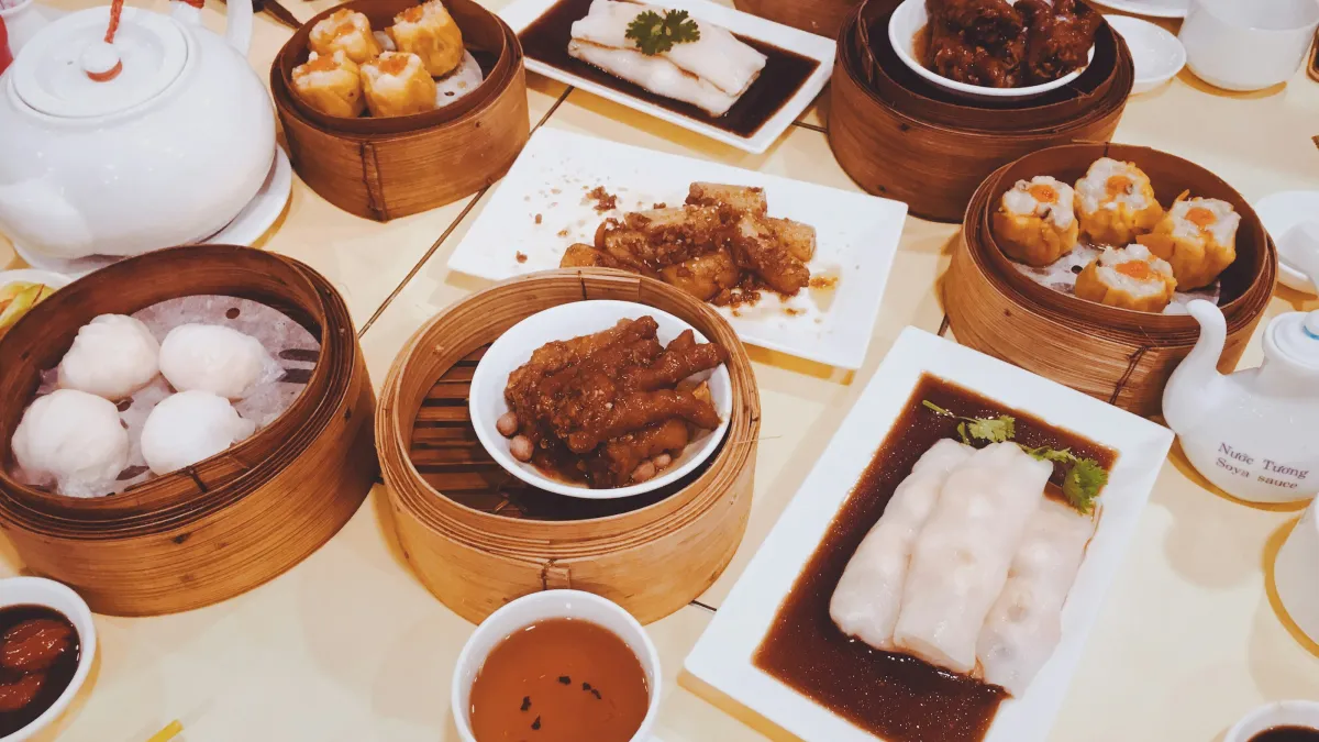 Variety of dim sum dishes served in bamboo steamers with tea and dipping sauces on a dining table.