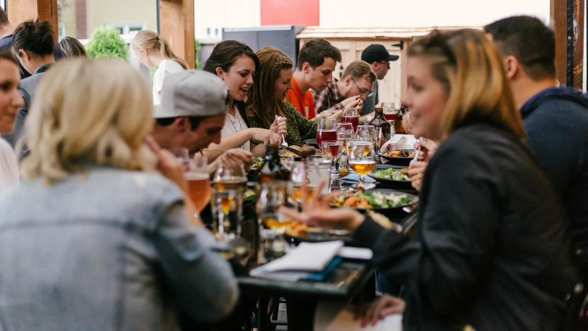 Group of people enjoying food and drinks together at an outdoor restaurant gathering.