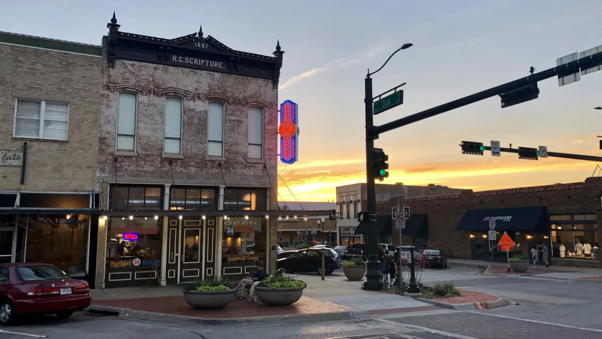 Historic brick building with neon sign at sunset on a small town street corner with traffic lights and parked cars.