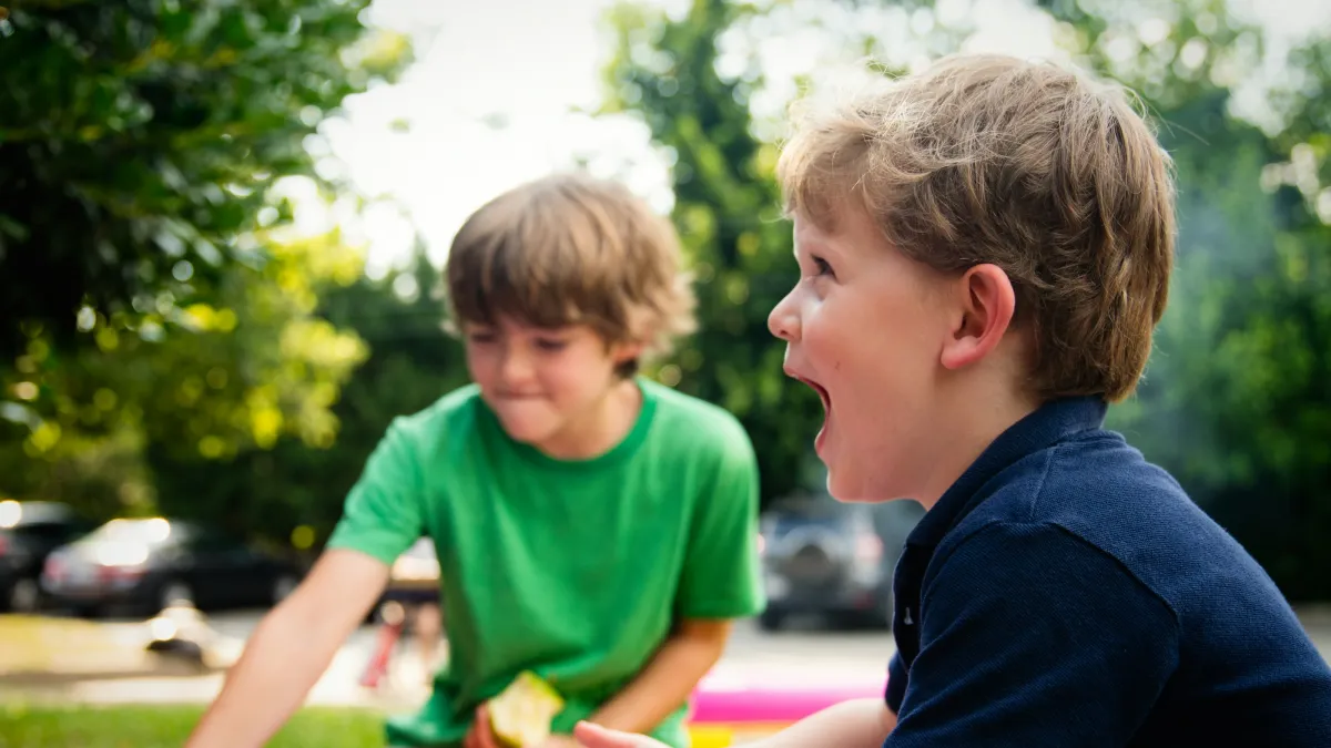 Two young boys playing excitedly by a pink inflatable pool outdoors on a sunny day.