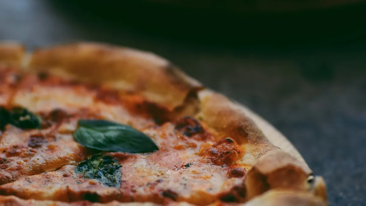 Close-up of a freshly baked margherita pizza with basil leaves on a dark surface, another pizza blurred in background