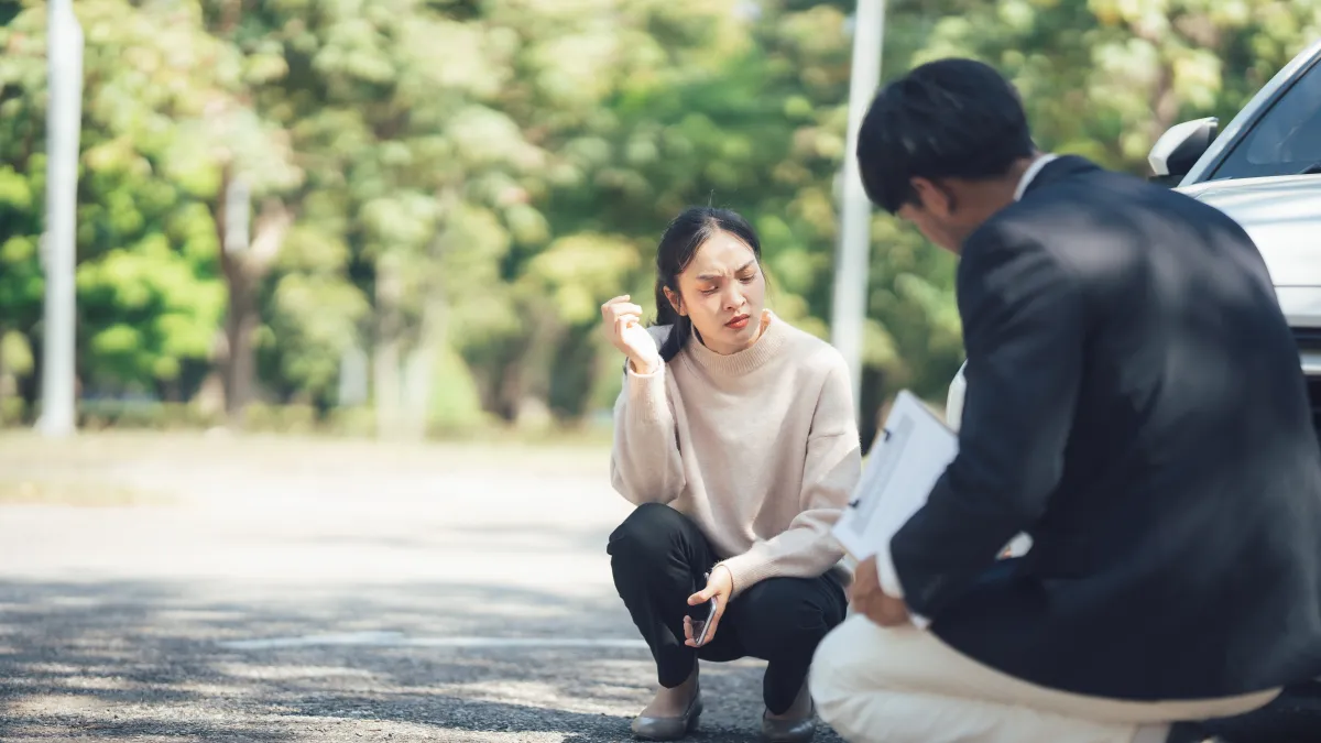 Woman and man crouching by a car examining damage during an insurance claim inspection outdoors