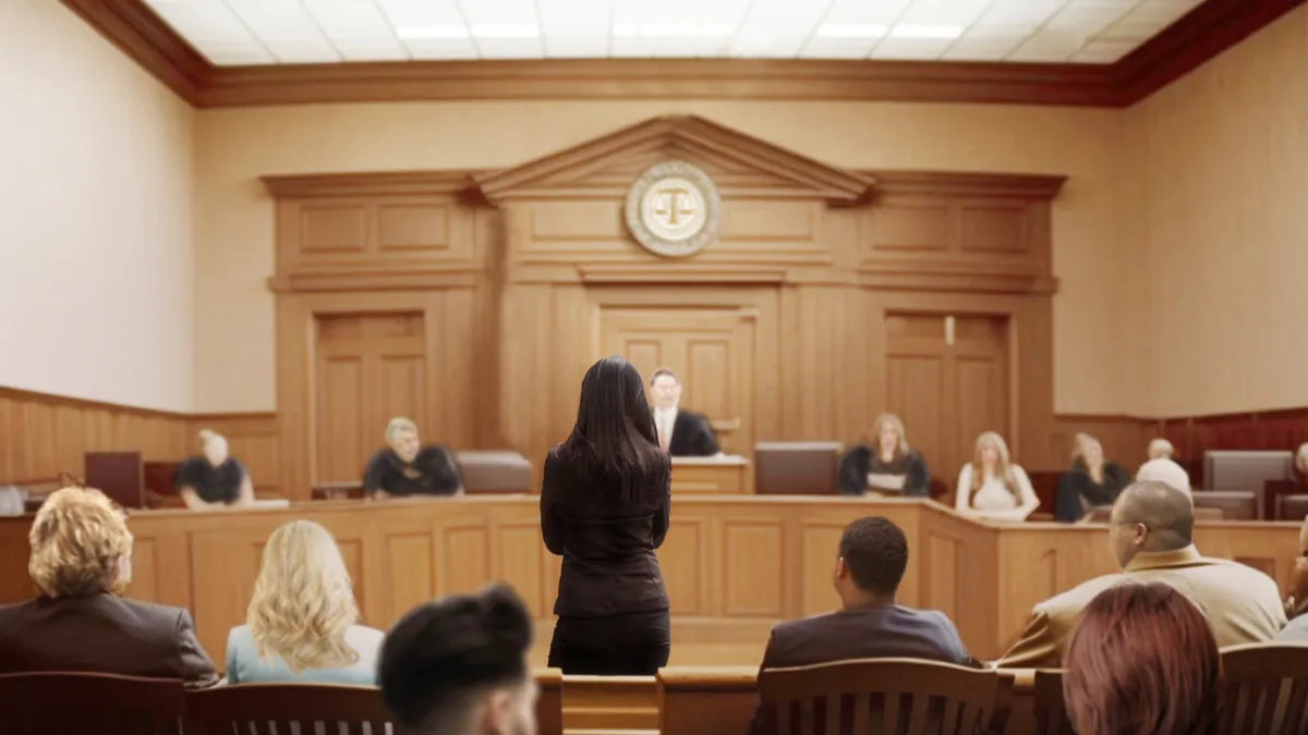 Lawyer standing and addressing judge in courtroom during a legal trial with jury and audience present