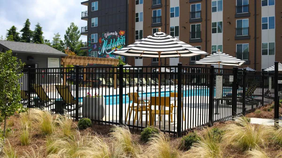 Apartment pool area with striped umbrellas, lounge chairs, and a 'Welcome to Mableton' mural on building.