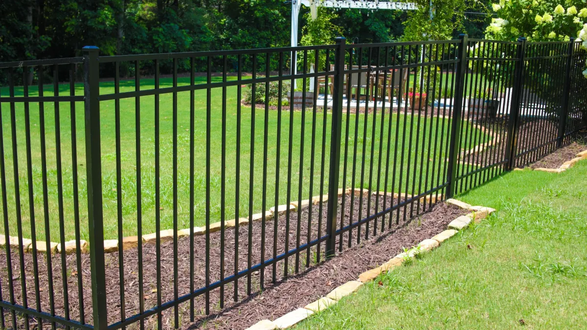 Black metal fence enclosing a landscaped backyard with green grass and a white wooden pergola in the background