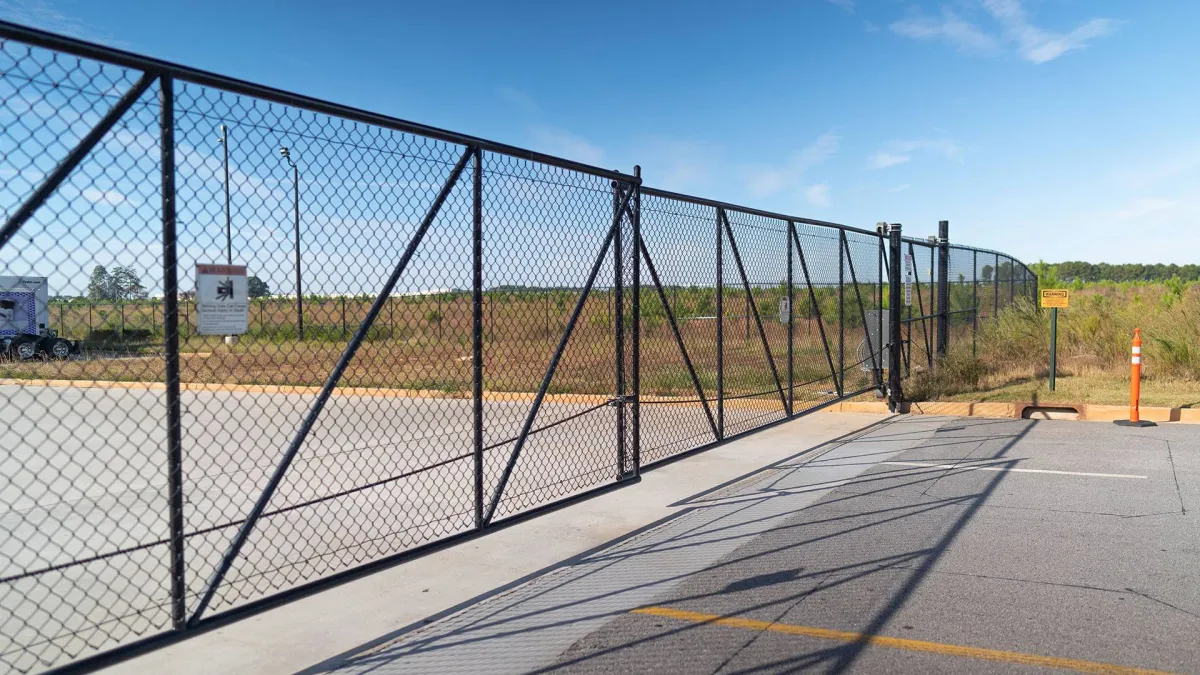 A black chain-link fence surrounds a vast open area under a clear blue sky.