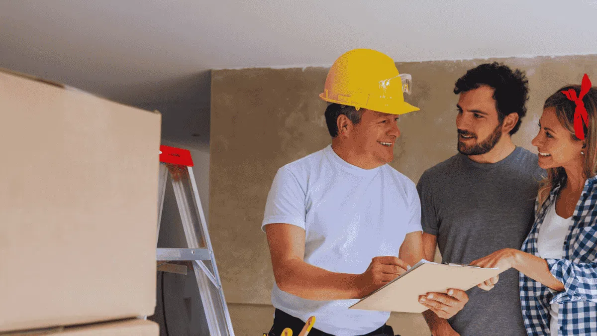 Contractor in yellow helmet discussing renovation plans with smiling couple inside unfinished home