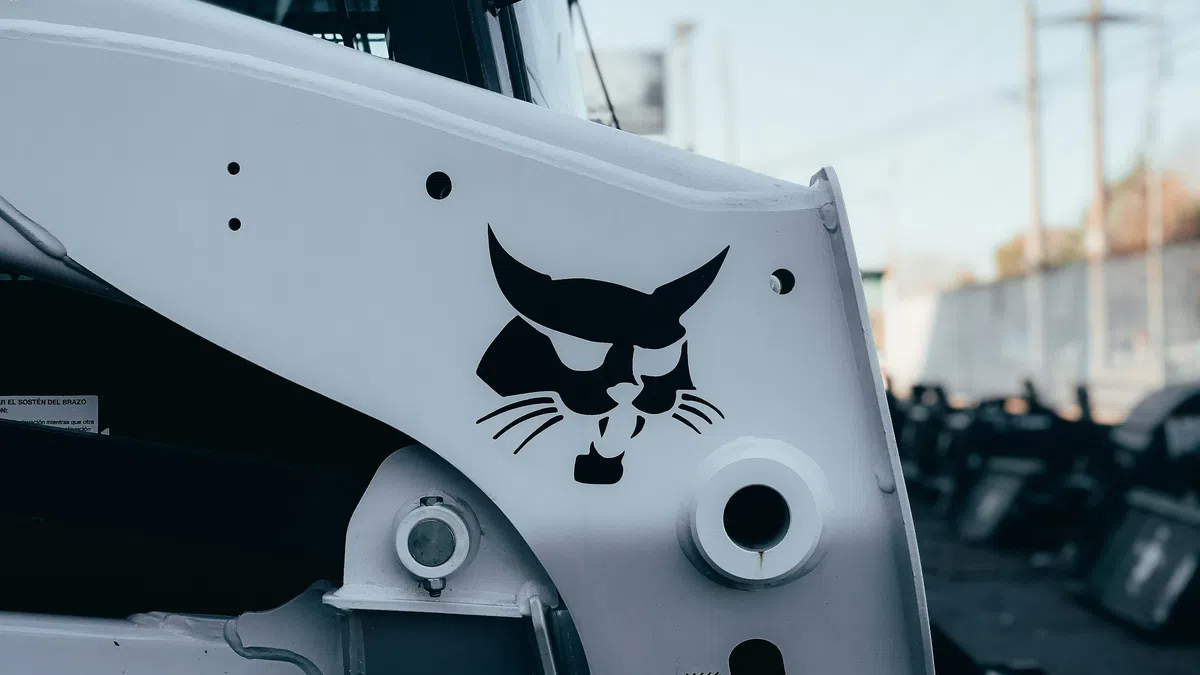 Close-up of a white construction vehicle featuring a black Bobcat logo on the side panel outdoors.