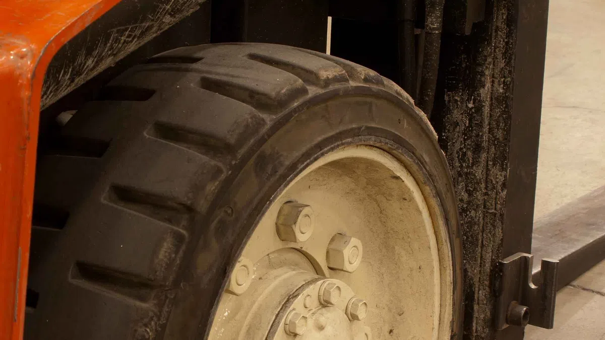 Close-up of a forklift tire and part of the lifting mechanism on a warehouse floor.