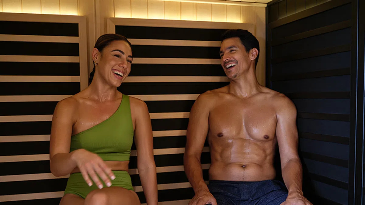 Smiling young man and woman relaxing and chatting inside a wooden sauna cabin.