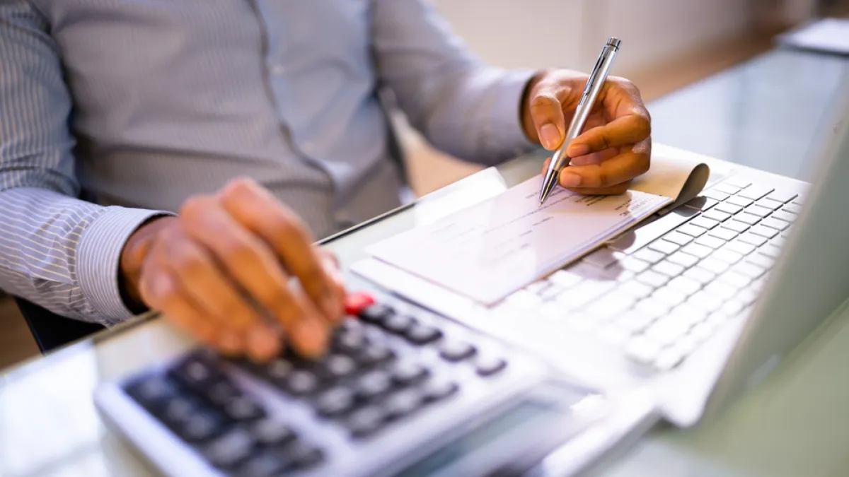 Person using calculator and writing on a check at desk with laptop