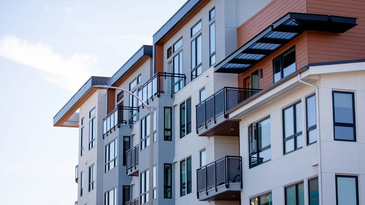 Modern multi-story apartment building with balconies and large windows under clear sky.
