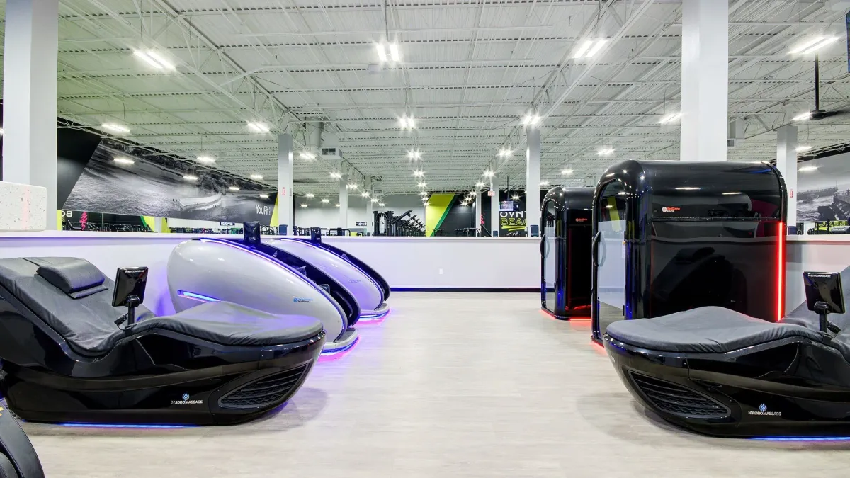 High-tech futuristic gym pods and relaxation chairs lined up in a bright, modern fitness studio.