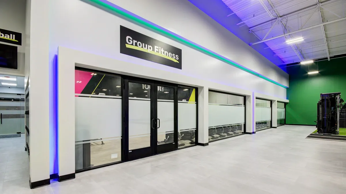 Modern group fitness room with glass doors, bright lighting, and spacious gym area with colorful accents.