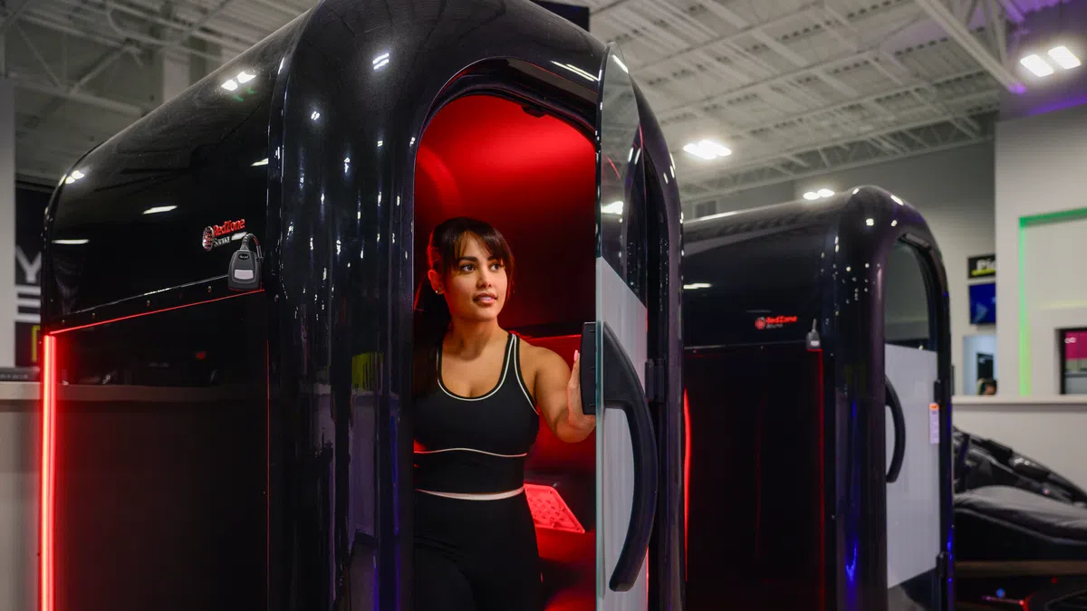 Woman exiting a black cryotherapy chamber with red interior lights in a modern gym setting