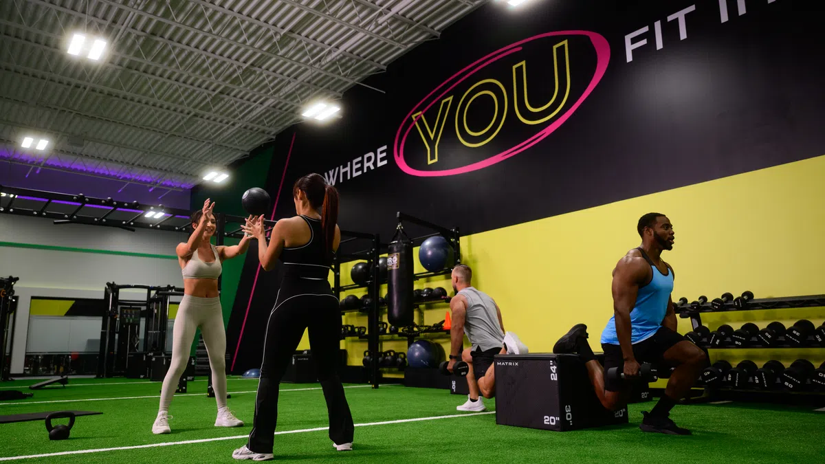 Four people working out in a gym with artificial turf and motivational wall text saying Where YOU Fit In.