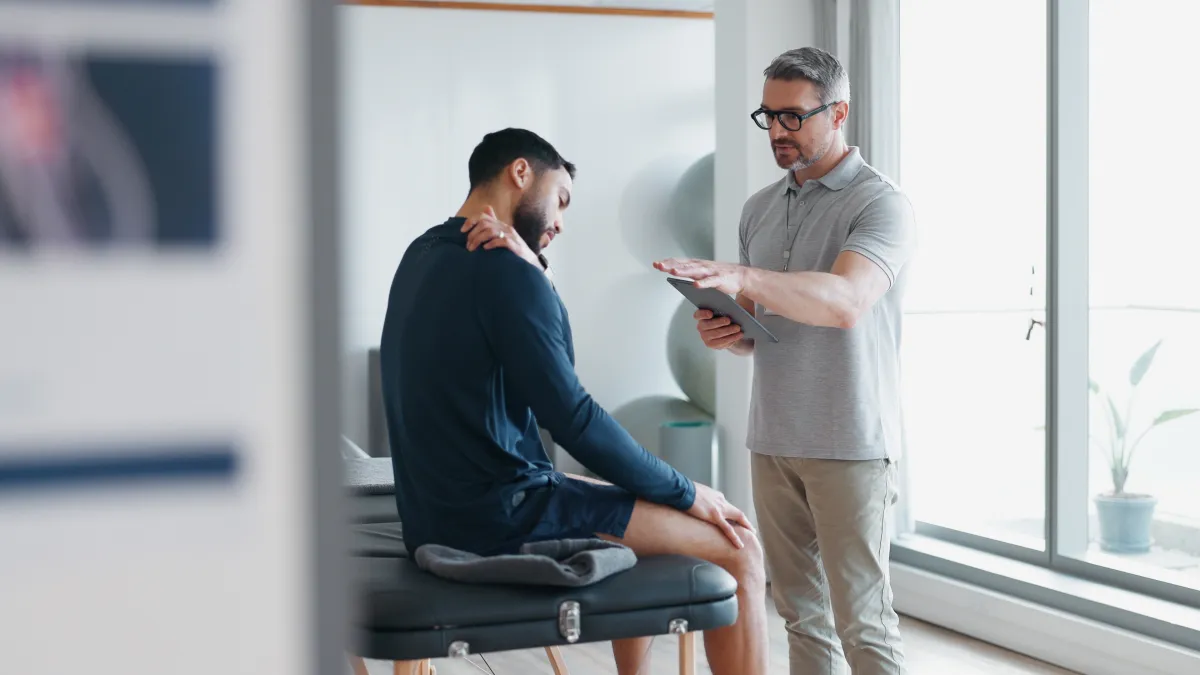 Physical therapist assessing a patient's shoulder pain during a clinic consultation in a bright room