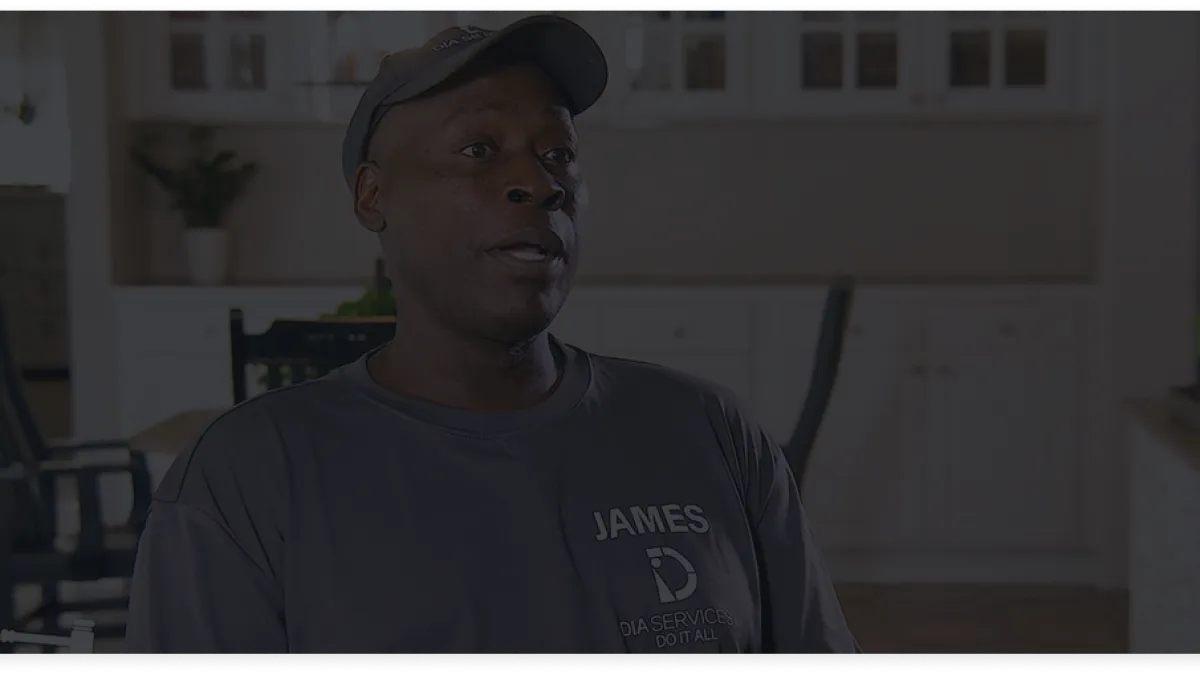 Man wearing a cap and a dark shirt with the name James and company logo in a bright kitchen setting.