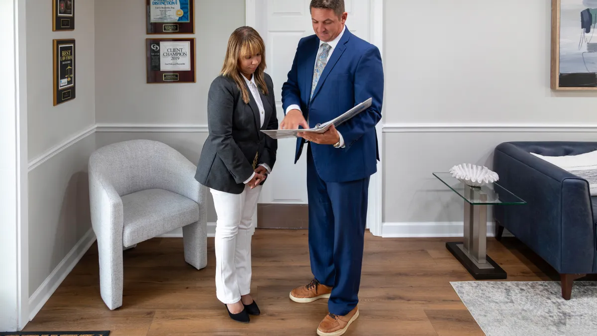 Businessman in blue suit showing documents to a woman in a gray blazer in a modern office setting.
