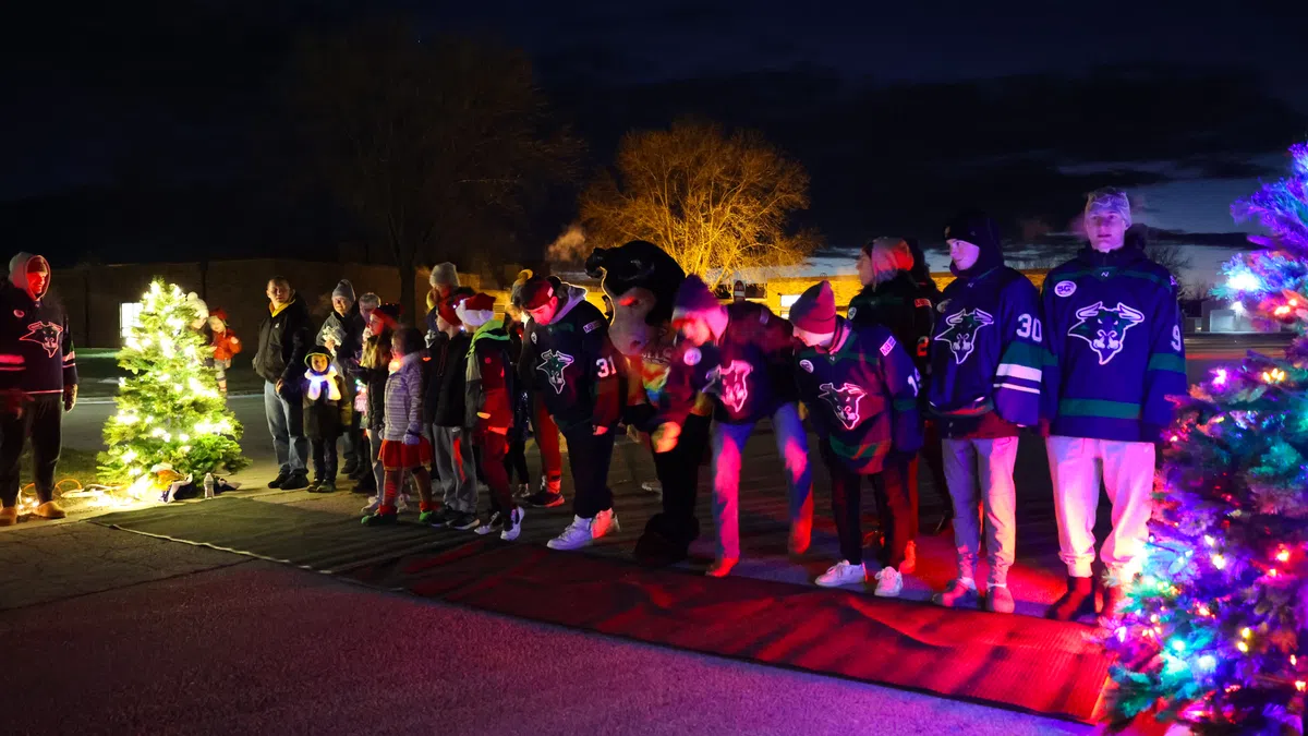 A festive scene with people in hockey jerseys celebrating under colorful lights and Christmas trees at night.