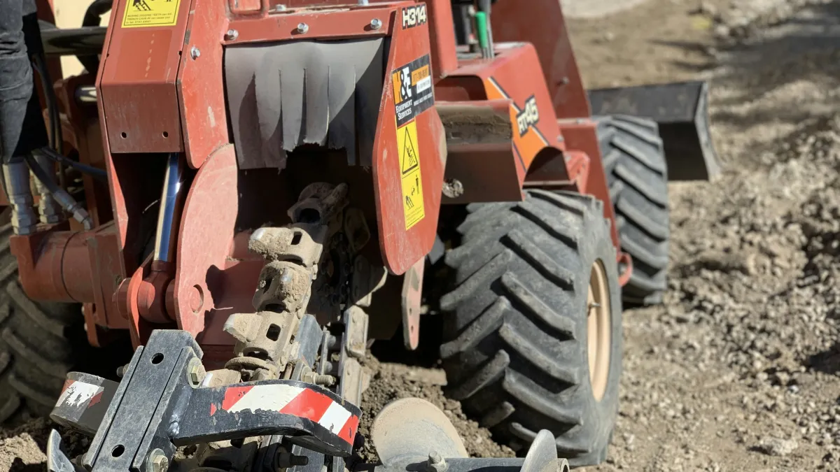 Close-up of a red trencher machine with large tires digging into dirt at a construction site.