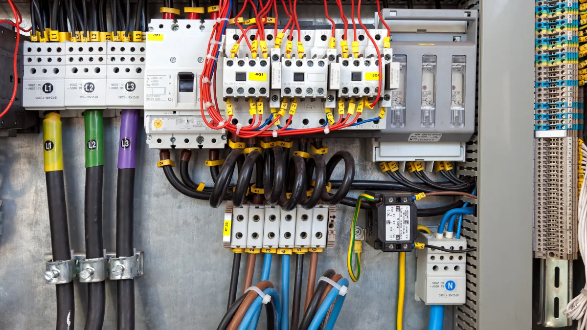 Electrical control panel with circuit breakers, labeled wires, and color-coded cables organized inside a metal enclosure
