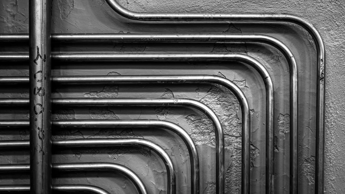 Black and white image of parallel metal pipes with right-angle bends on a textured wall.