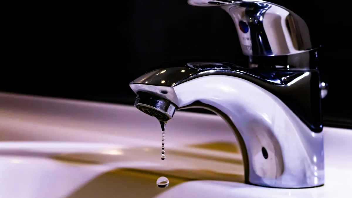Close-up of a dripping chrome faucet over a white sink with water droplets falling