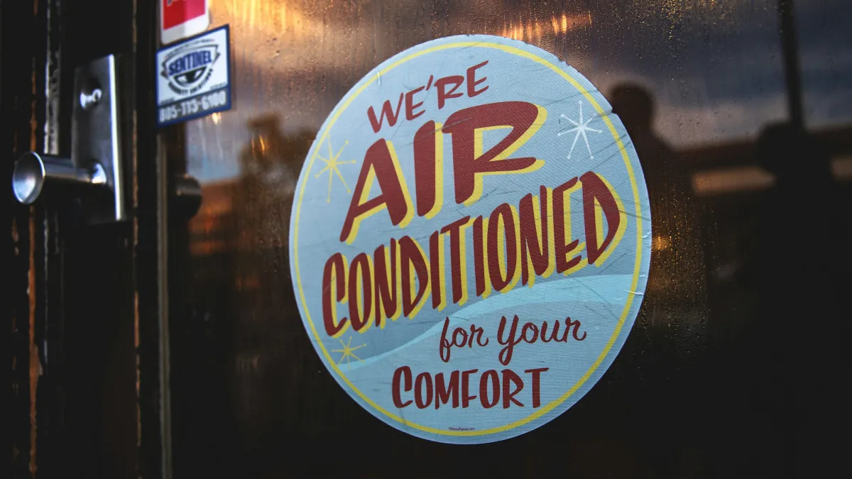 Round sign on glass door stating We're air conditioned for your comfort with warm light reflections.