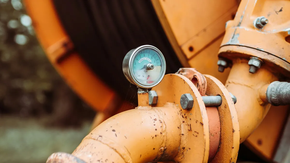Close-up of an orange industrial pipe with pressure gauge and bolts on machinery outdoors.