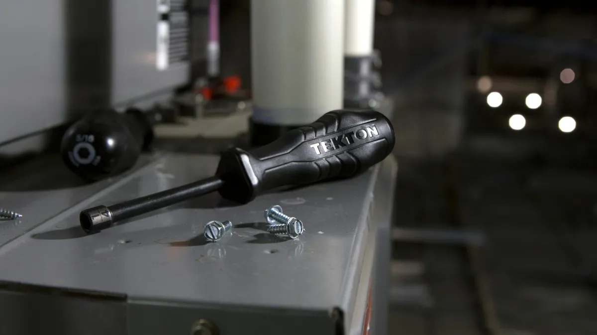 TEKTON screwdriver and screws on metal surface in workshop with blurred background tools and equipment.