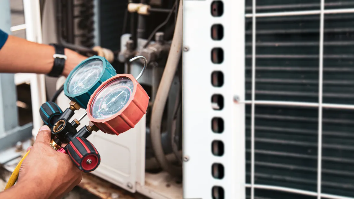 Technician checking HVAC system pressure with dual gauge manifold for air conditioning maintenance and repair.