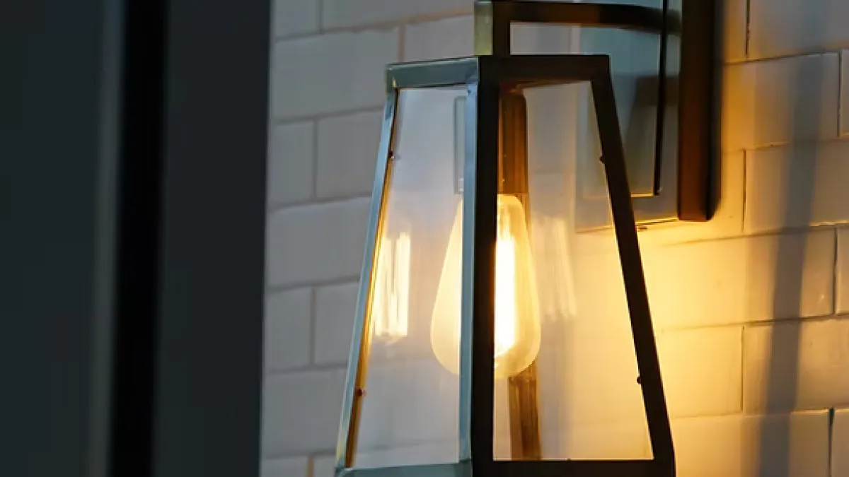 Modern wall-mounted lantern with a glowing bulb illuminating white subway tile wall in soft warm light