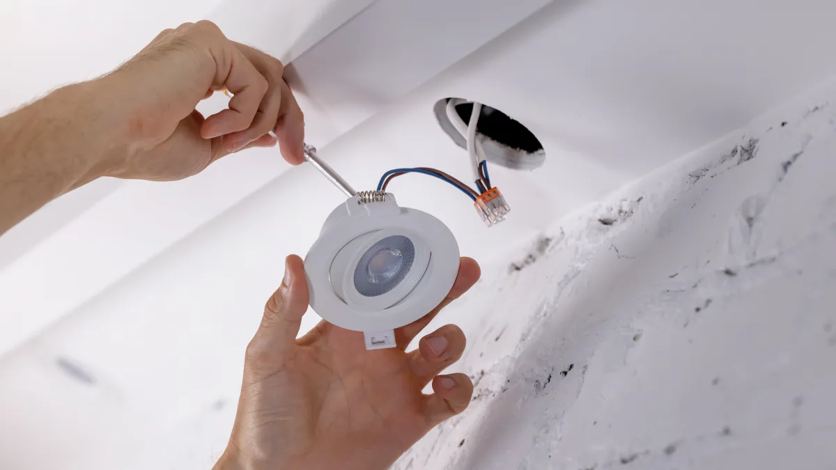 Hands installing a round LED recessed light fixture into a ceiling with wiring visible