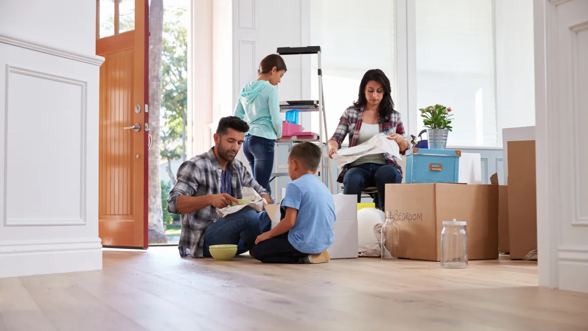 Family unpacking boxes and organizing belongings in a new home with natural light and wooden floors.