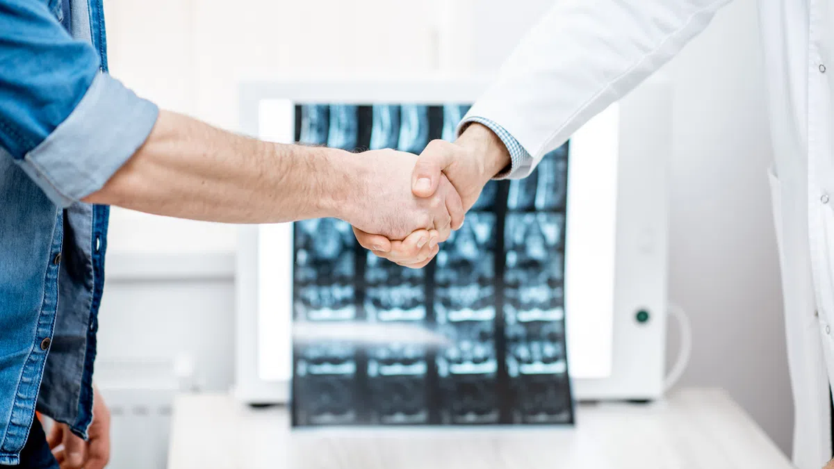 Doctor and patient shaking hands with spinal X-rays in background in medical office setting