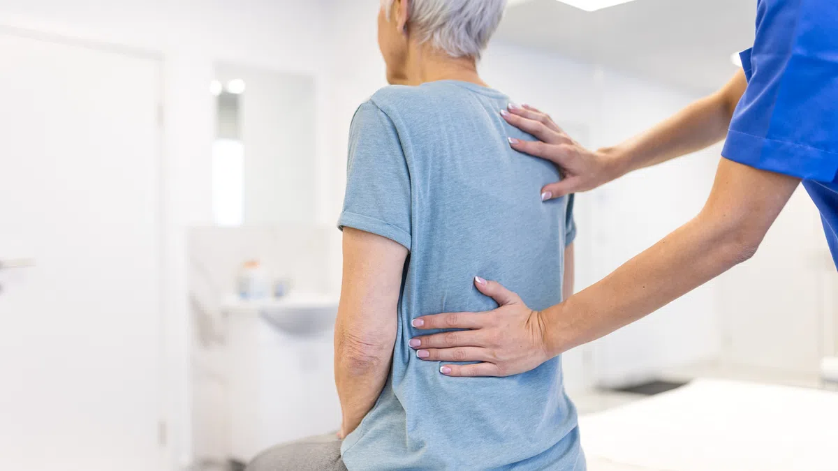 Healthcare professional assessing elderly woman's back in a bright medical office setting.
