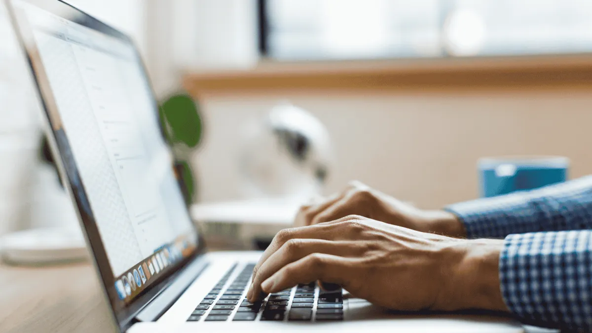 Hands typing on a laptop keyboard with a blurred background in a bright workspace.