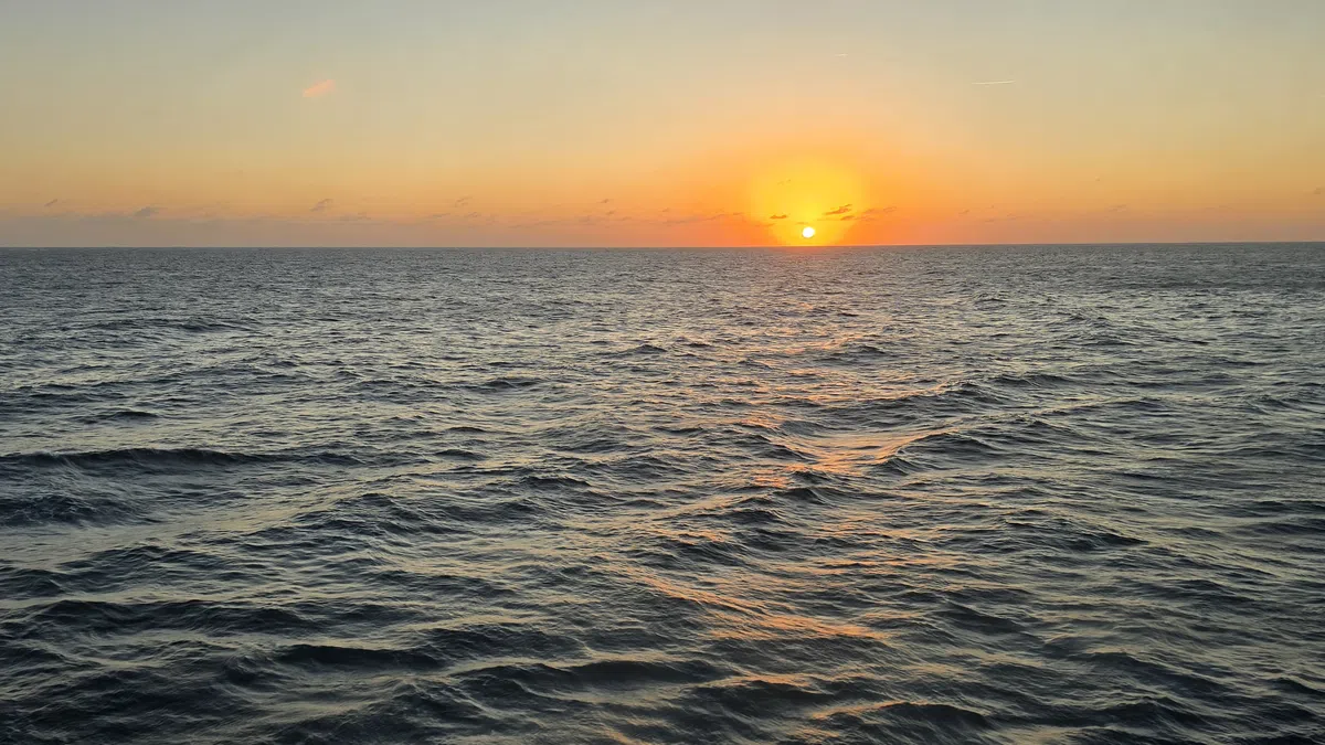 Sunset over a calm ocean with clear sky and rippling water reflecting orange sunlight.