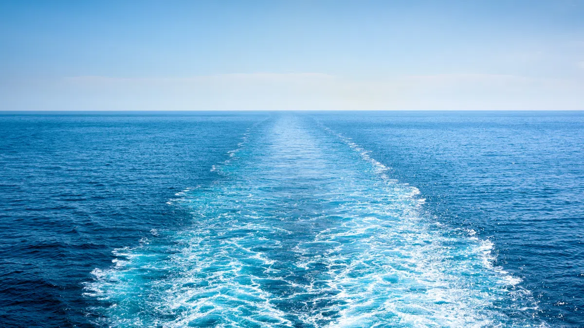 Clear blue ocean with a visible wake trail extending into the horizon under a bright sky