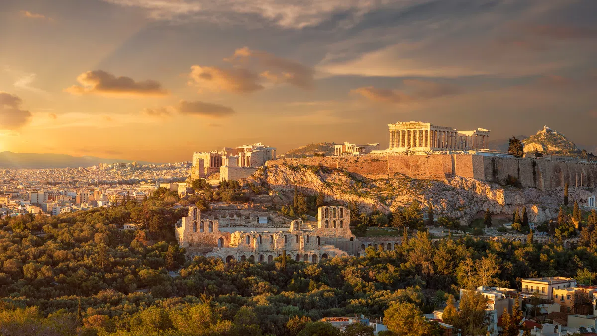 Sunset view of the Acropolis of Athens with the Parthenon and surrounding ancient ruins in golden light.