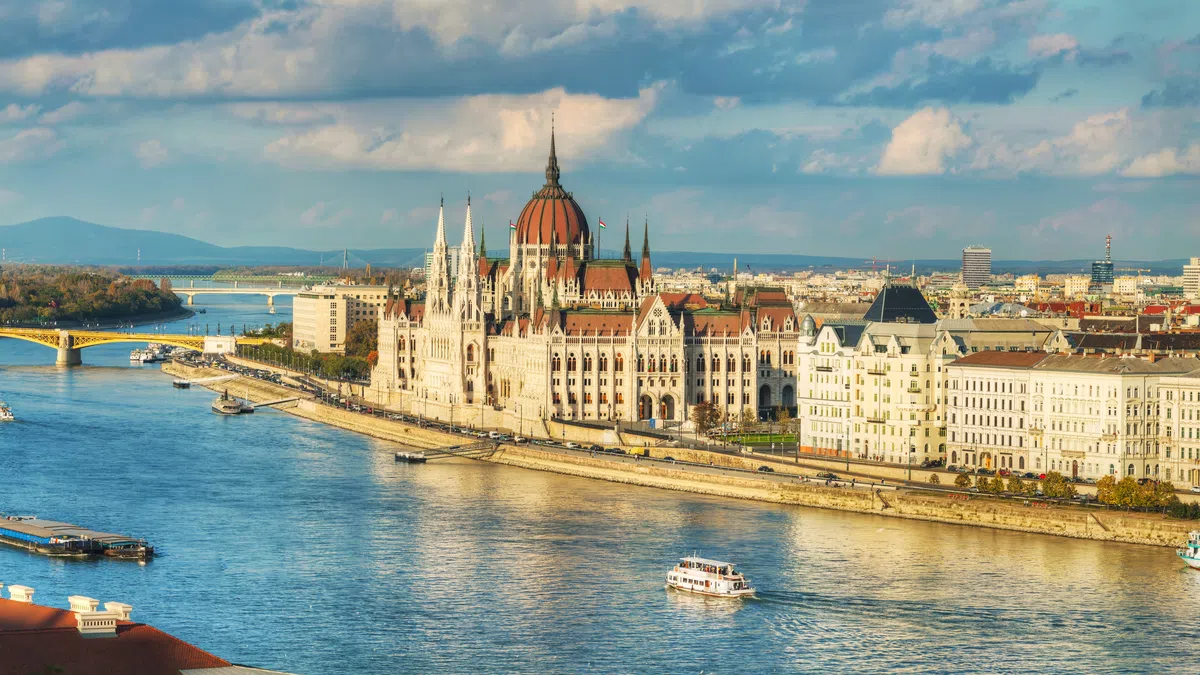 Panoramic view of the Hungarian Parliament building by the Danube River in Budapest with boats and cityscape.