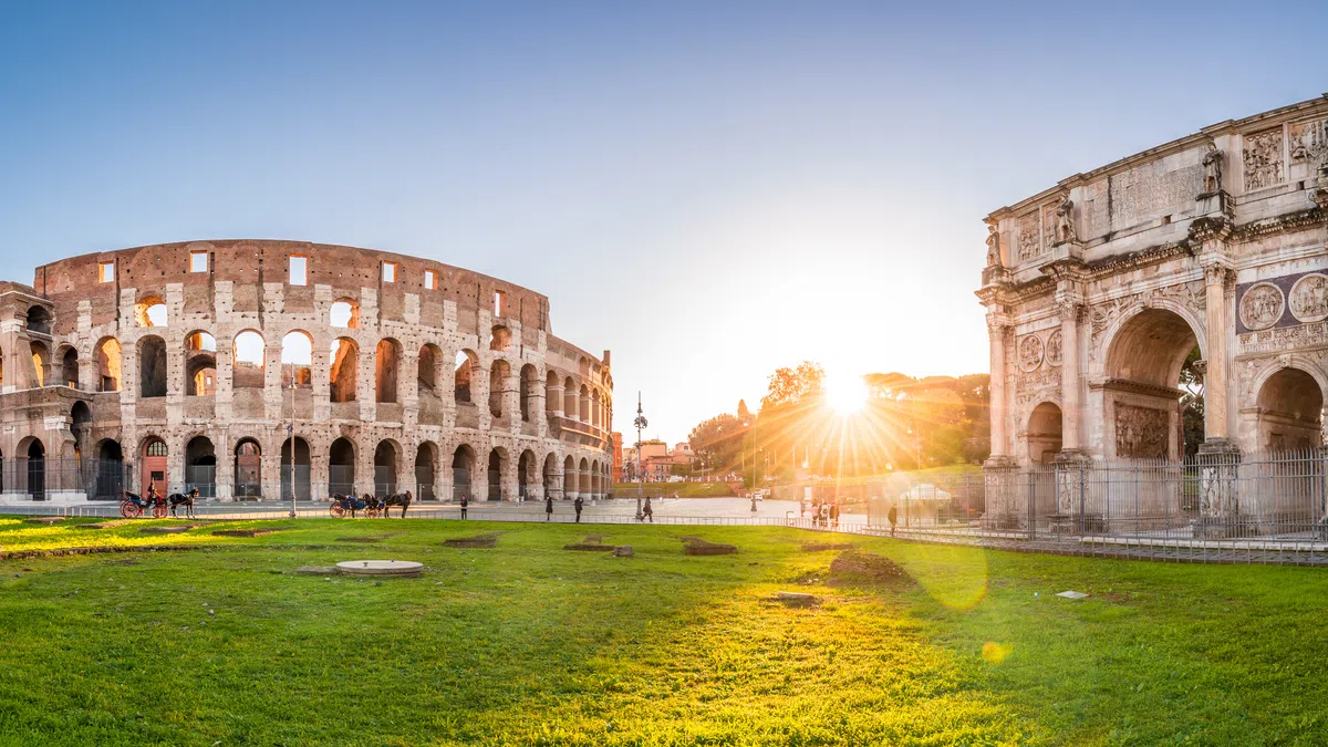 Sunset view of the Colosseum and Arch of Constantine in Rome with green grass and clear skies.