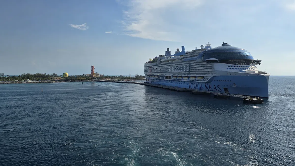 Large cruise ship docked near tropical island with blue sky and calm ocean waters