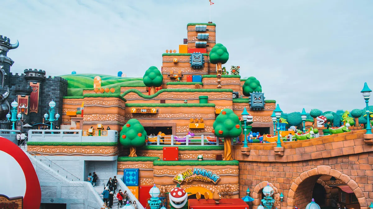 Colorful Super Mario-themed amusement park with blocky hills, trees, characters, and visitors exploring the area.