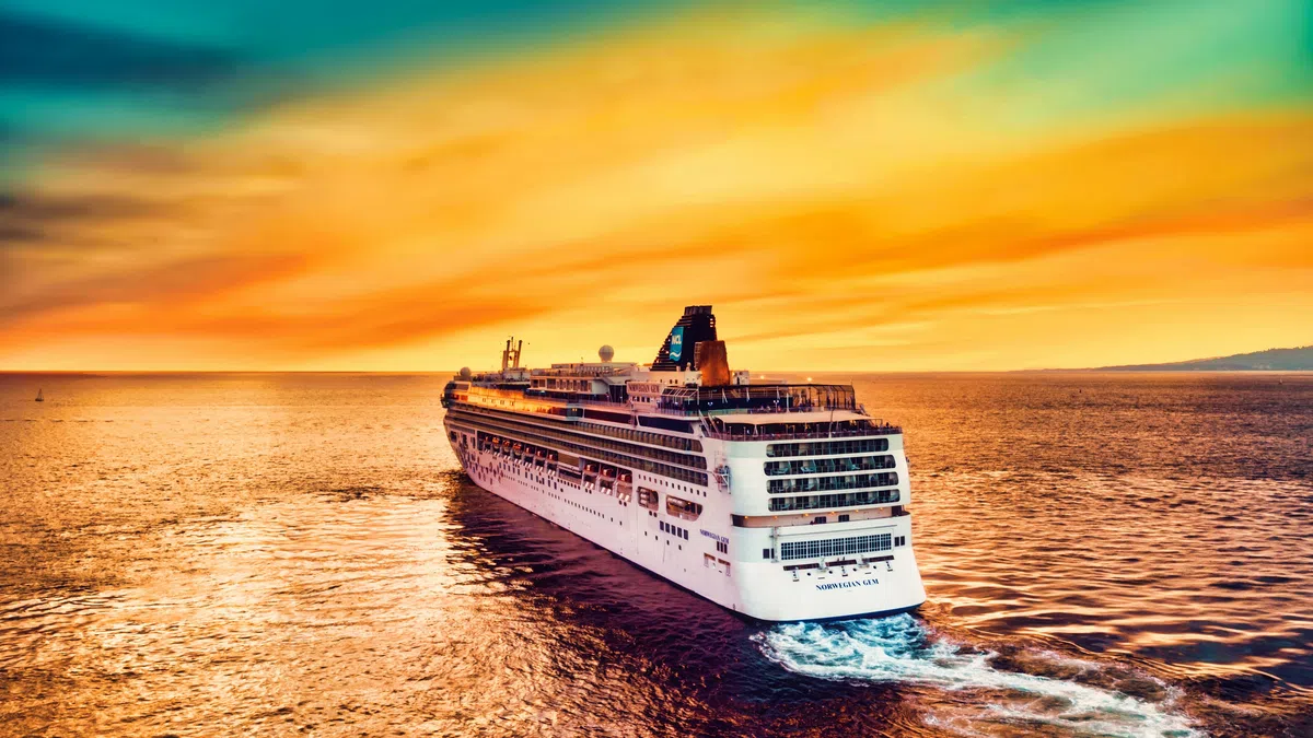Large cruise ship sailing on calm ocean waters during a vibrant orange and yellow sunset.