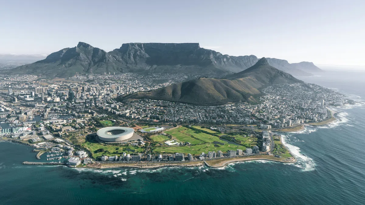 Aerial view of Cape Town with Table Mountain, Lion's Head, cityscape, and coastal shoreline under a clear sky.