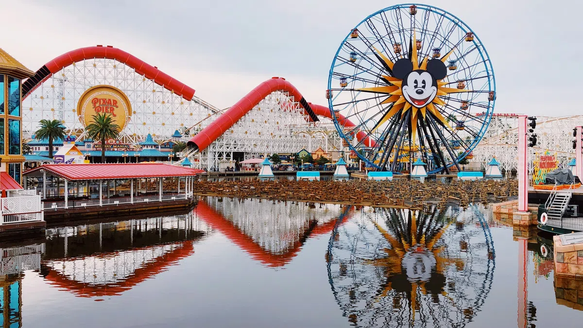 Mickey Mouse Ferris wheel and red roller coaster reflected in water at Pixar Pier amusement park.